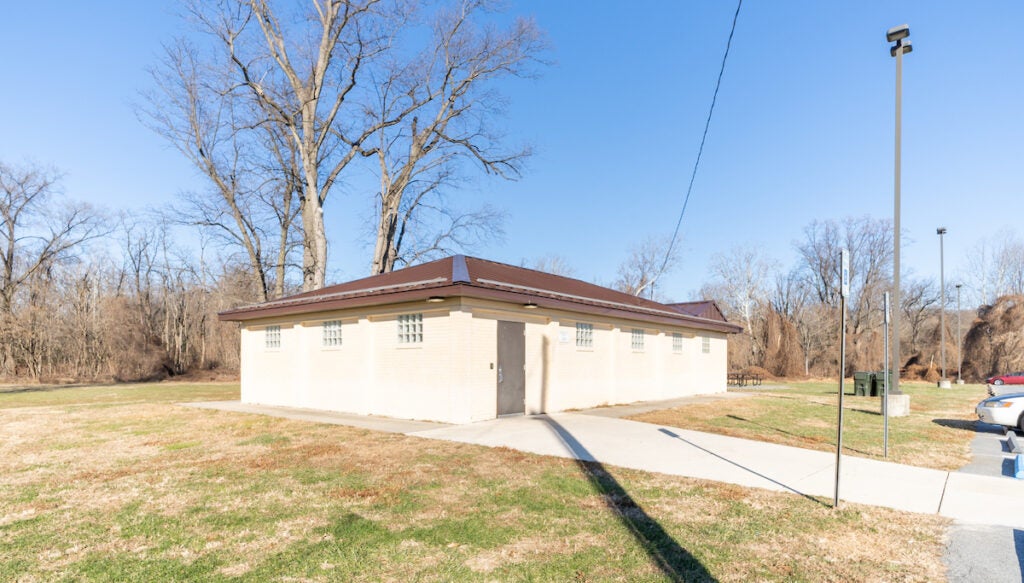 Exterior of a small, single-story beige building with a sidewalk leading to the door.