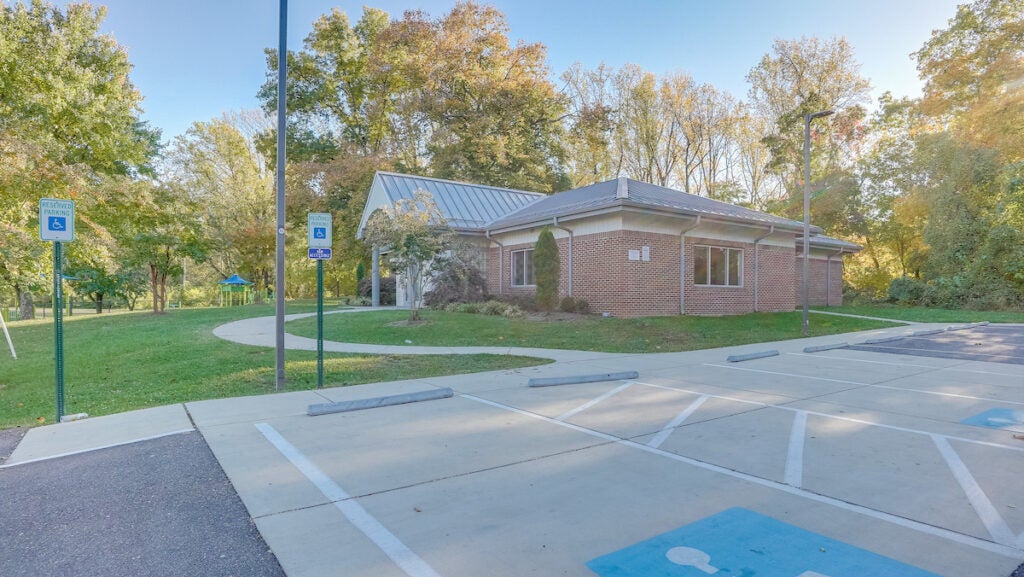 Exterior view from the parking lot of a single-story brick building with a peaked portico over the entrance.