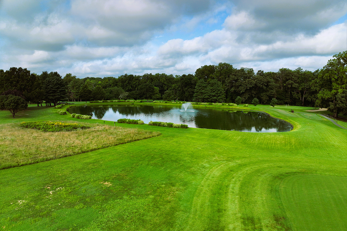 The pond at Enterprise Golf Course. There is a fountain in the middle of the pond, and one of the hole tees off to the right, surrounded by bright green grass.