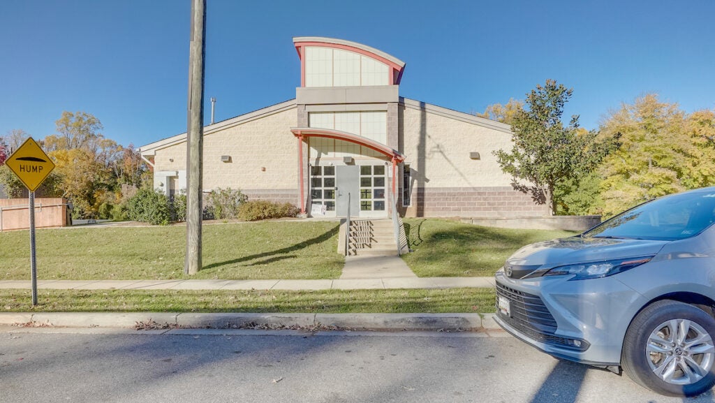 Exterior view of a contemporary, beige, concrete building with a peaked roof and a portico over the entrance.