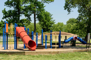 A colorful outdoor playground with a red slide. In the background is a single-story yellow building.