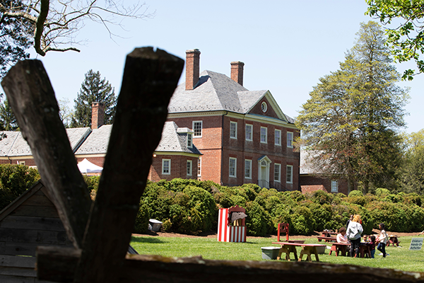 A manor in the distance, with tables and people playing on the front lawn