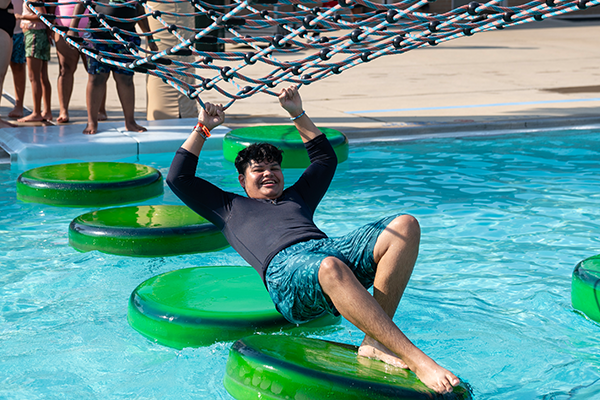 A boy crossing a pool with the help of a ladder and floating foam lilypads
