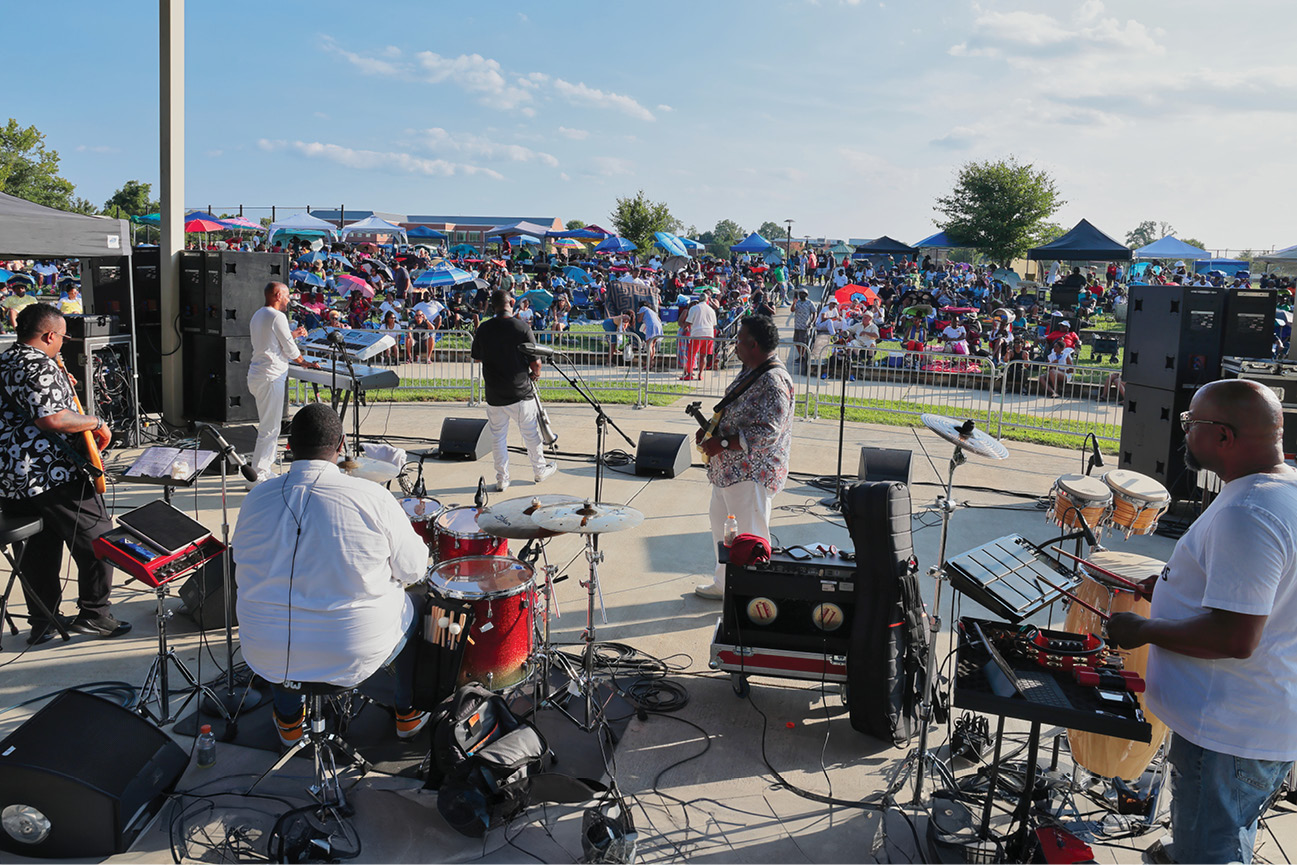 A band of musicians playing for a crowd sitting on the grass
