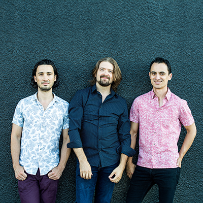 Three men in button-up shirts against a rough textured blue wall