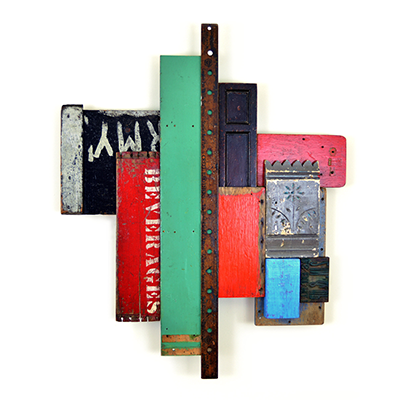 A wall sculpture that appears to be comprised of various painted boards, metal scrap, and other items, combined into an assemblage. The boards are painted green, red, blue, and black.