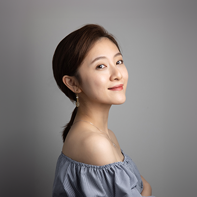 A person smiling towards the camera, against a gray background