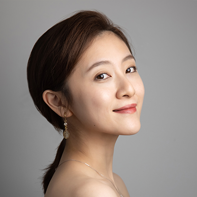 A person smiling towards the camera, against a gray background