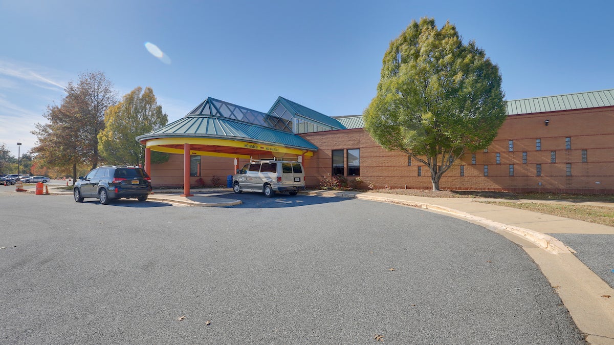 Exterior view of a large brick, glass, and metal building with a blue and yellow portico supported by red columns.