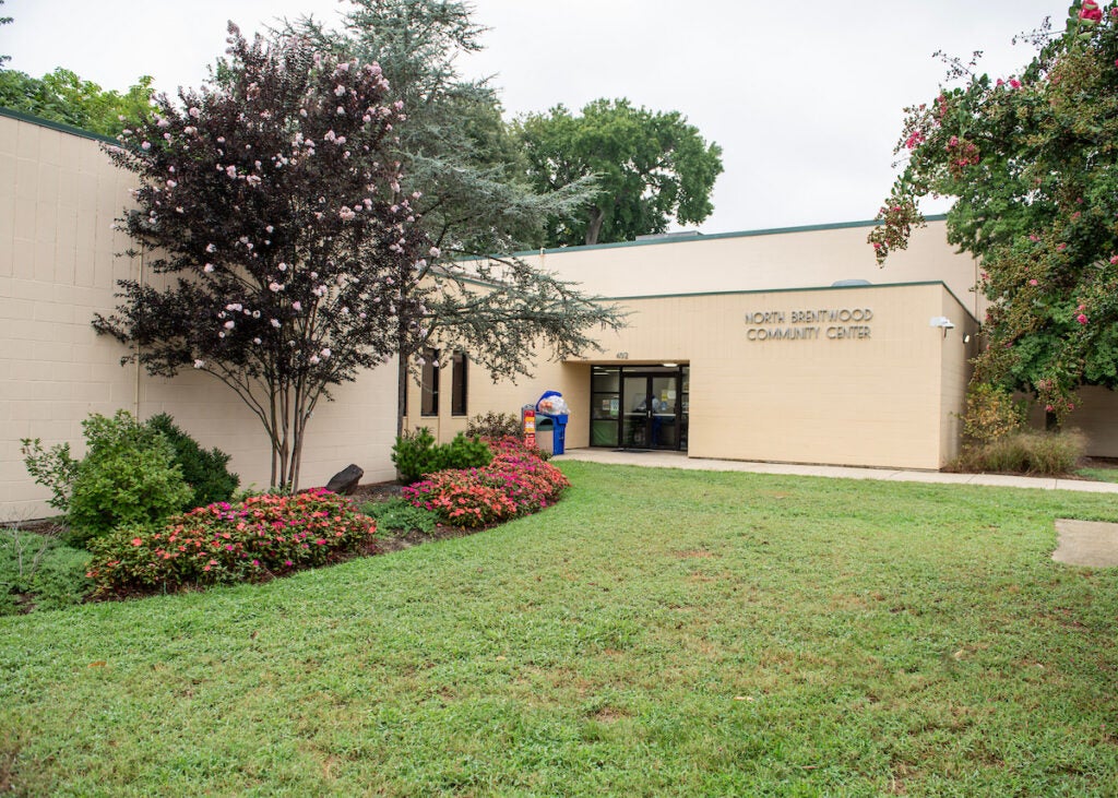 The entrance to a large, beige, cinderblock building with green trim. Letters on the building spell out NORTH BRENTWOOD COMMUNITY CENTER.