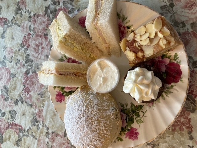 An assortment of sandwiches and pastries served on a floral plate.