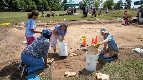 A group of four individuals with buckets and pales digging in the dirt