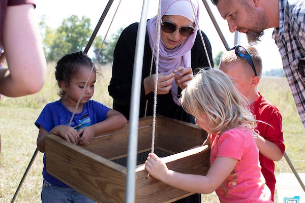 A woman in shades and three children looking into a wooden box