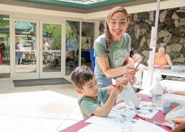A parent and child at an arts and crafts table set up outside a building entrance.