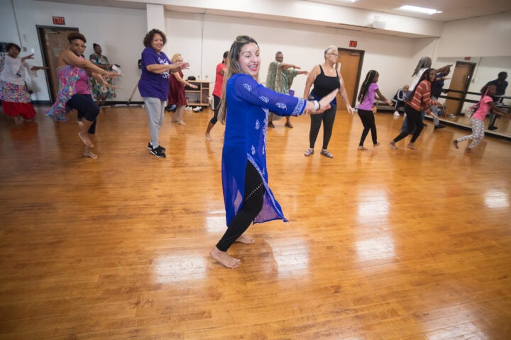 A woman in traditional attire is teaching a group of people how to dance in a fitness studio.