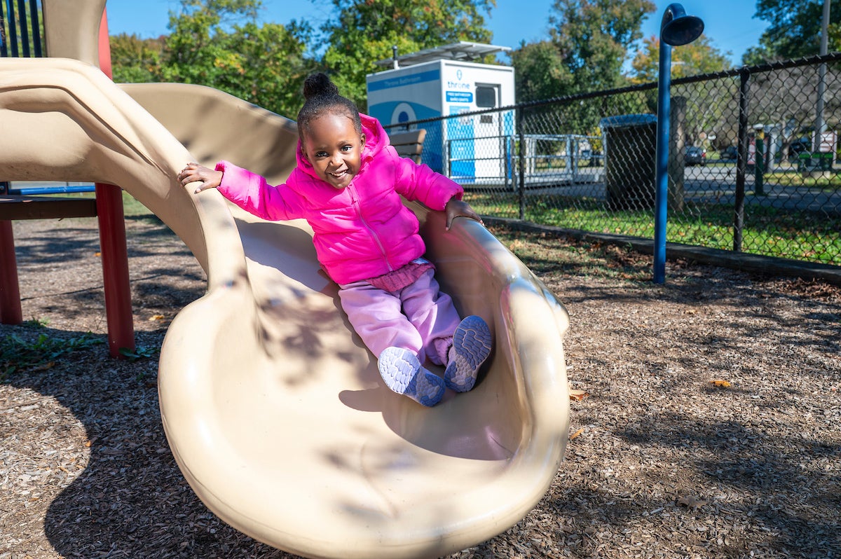 A smiling kid plays on a slide at a a playground.