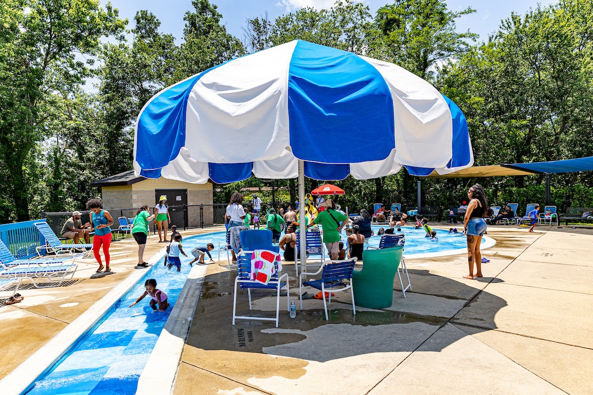 A circular kiddie pool with a long entrance ramp and a giant shade umbrella nearby.