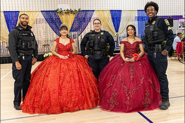 Three Park Police officers standing next to two girls in red dresses at a quinceanera taking place in a gymnasium