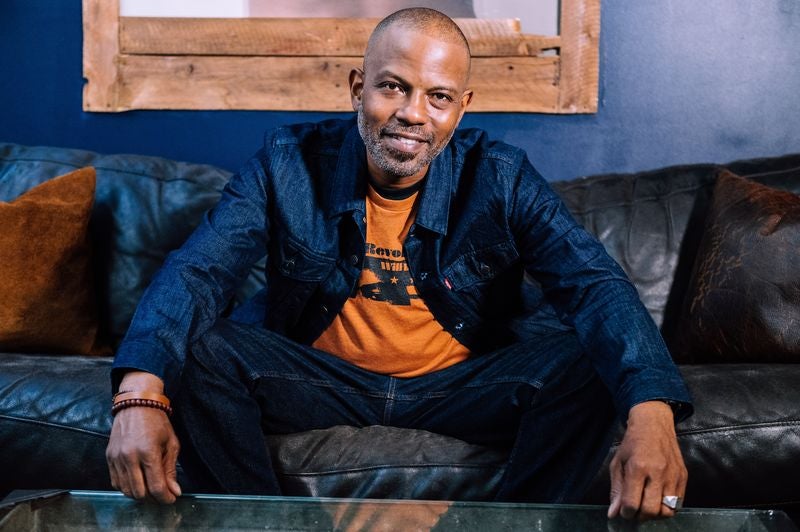 Person seated on leather couch in denim outfit, smiling slightly in studio-style portrait.