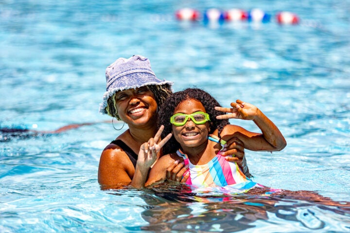 A woman holding a small girl pose for the camera in an outdoor pool.