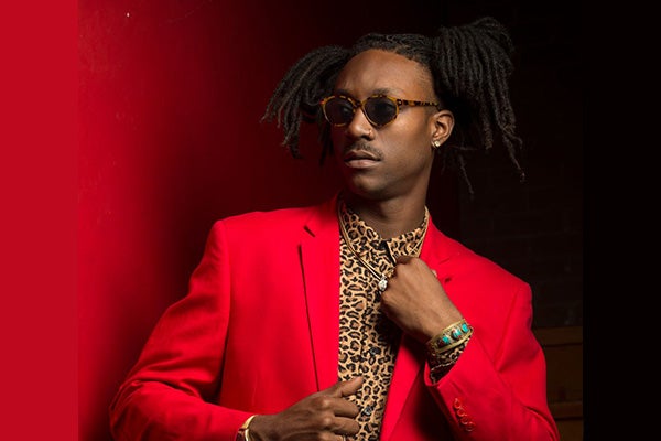 Promotional headshot of a man in a red jacket and leopard-print shirt, wearing sunglasses.