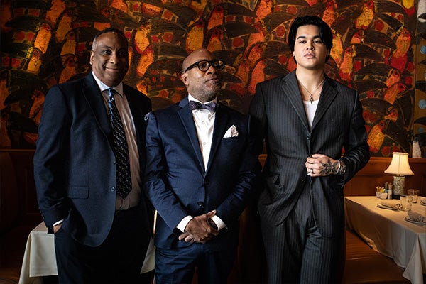 Three men in suits pose in a restaurant.