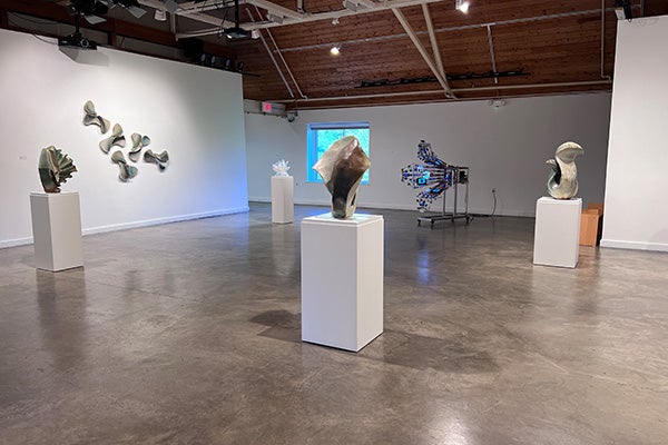 Sculptures on display in an art gallery with white walls and a peaked, wooden ceiling.