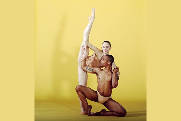 Two dancers wearing nude leotards strike a dramatic pose on a stage.