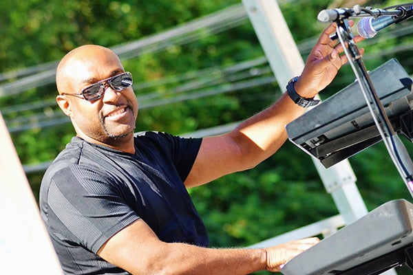 A man in black plays multiple keyboards in the sunshine.