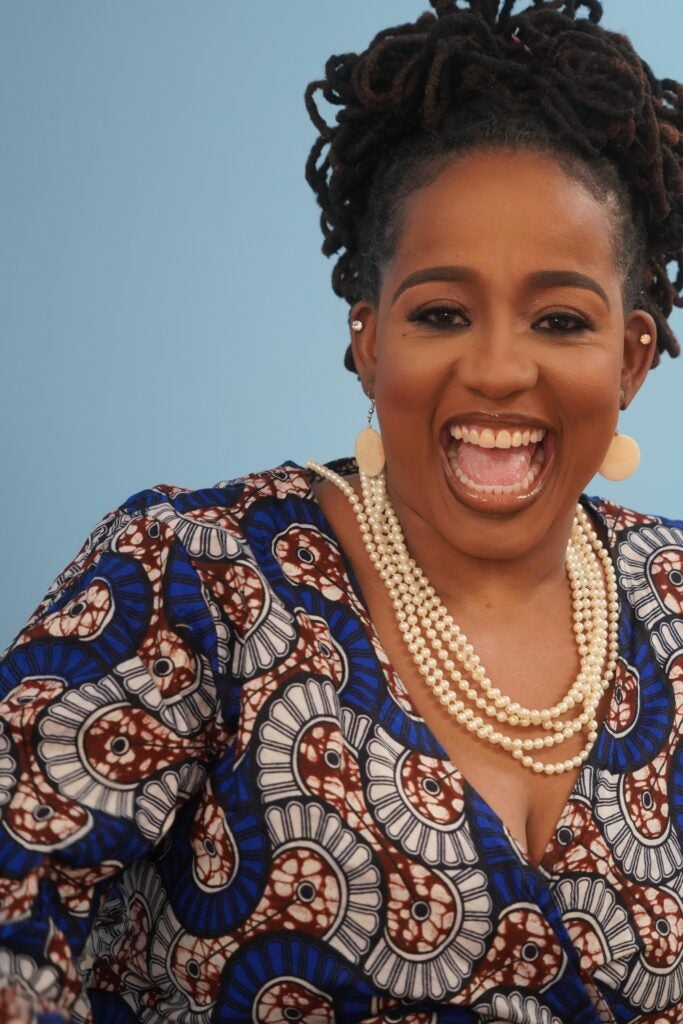 Portrait of a person wearing a blue-and-white patterned outfit and pearl necklace against a light blue background.
