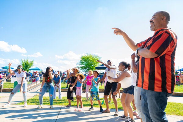 A group of individuals of various ages dancing outdoors in an amphitheatre.