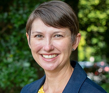 Headshot of a smiling woman with short hair, wearing a blue jacket over a yellow and white shirt.