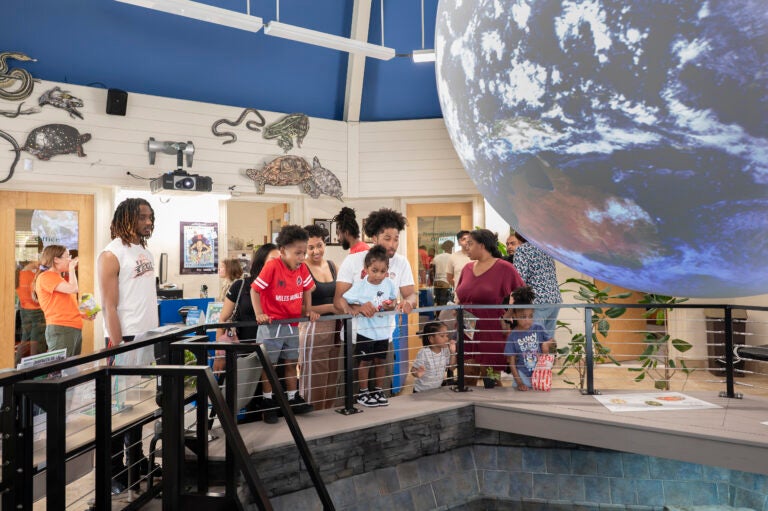 Museum visitors gather around a large suspended globe exhibit, viewing interactive displays and educational exhibits inside a nature center.