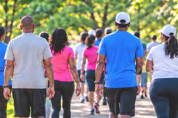 People with athletic clothing taking a walk along a path with lots of trees and greenery around them.